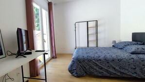 Een slaapkamer met een bed, een bureau met een computer, een stoel en een raam met gordijnen.