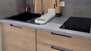 Een moderne keuken met een zwarte spoelbak, houten keukenkastjes, een rvs afzuigkap en een geïntegreerde kookplaat.
