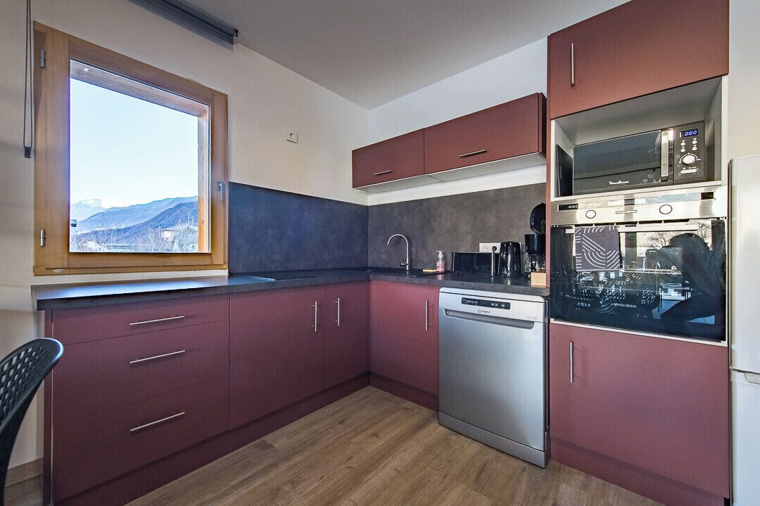 A compact kitchen with a dishwasher, microwave, and oven. A window offers a view of the outdoors.