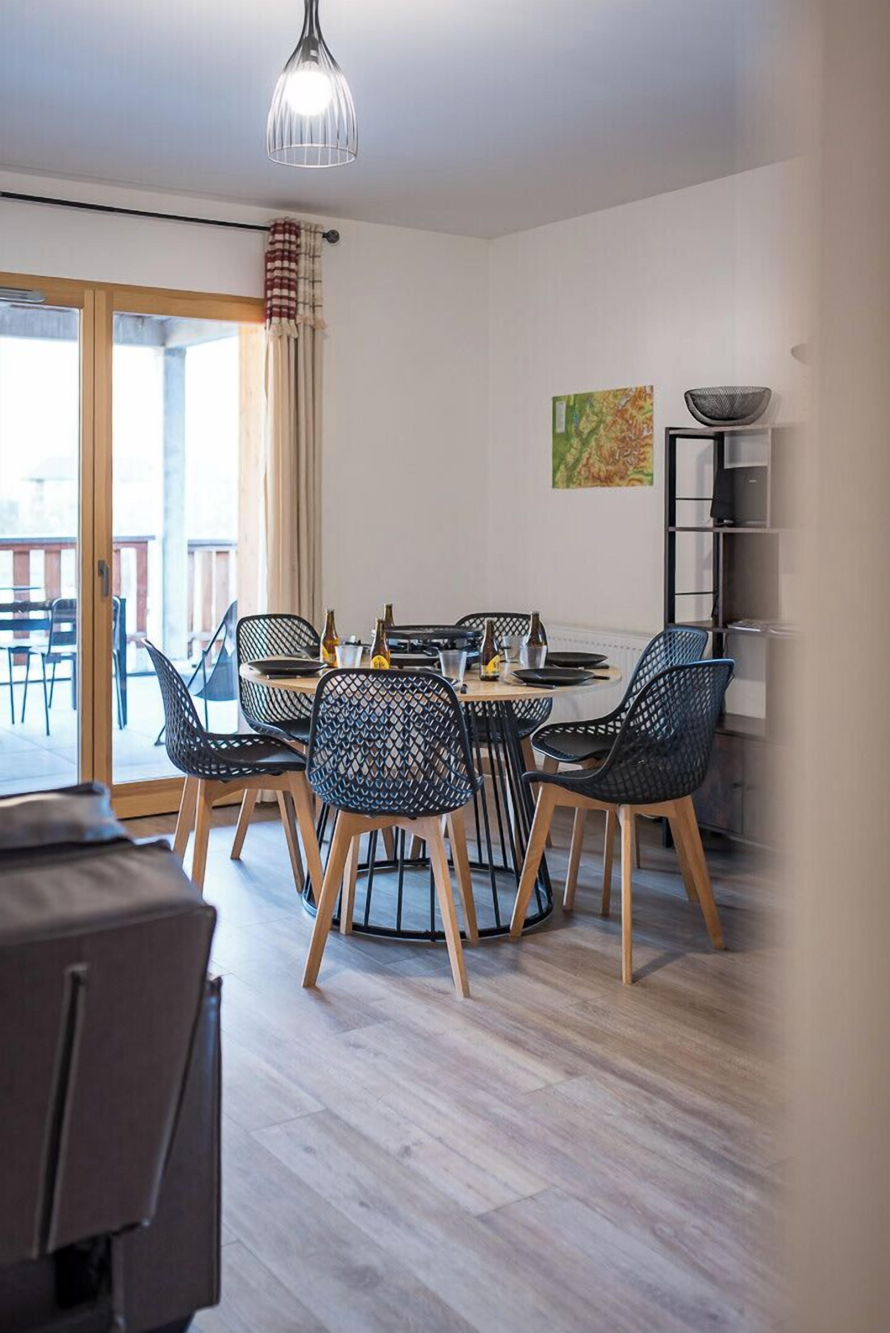 A modern dining area with a round table, black chairs, and a hanging light fixture.