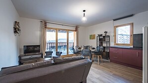 Ein modernes Wohnzimmer mit Sofa, Fernseher, Essbereich und Küche.