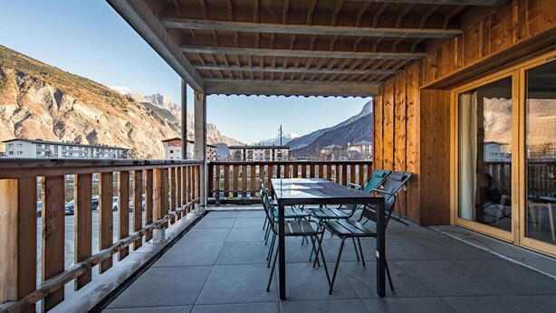 Ein Holzbalkon mit Tisch und Stühlen mit Blick auf eine Berglandschaft.