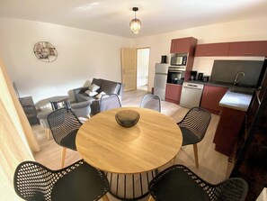 Cozy living area with a round dining table, grey sofa, and kitchenette featuring a microwave, oven, and sink.