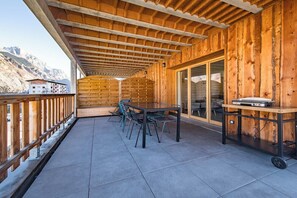 A wooden deck with a table and chairs, a sliding glass door, and a view of mountains.