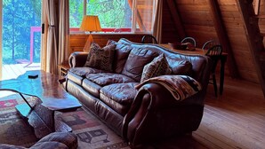 A cozy loft-style room with a leather sofa, a small table, and a view of the outdoors. - A-frame cabin tucked in the woods with complete privacy in the mountains.   (De Borgia)