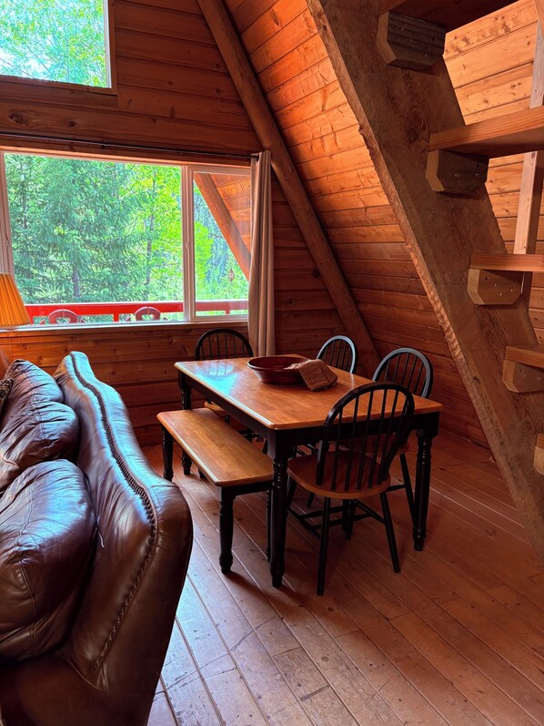 A cozy cabin interior with a wooden dining table, four chairs, a bench, and a leather couch.