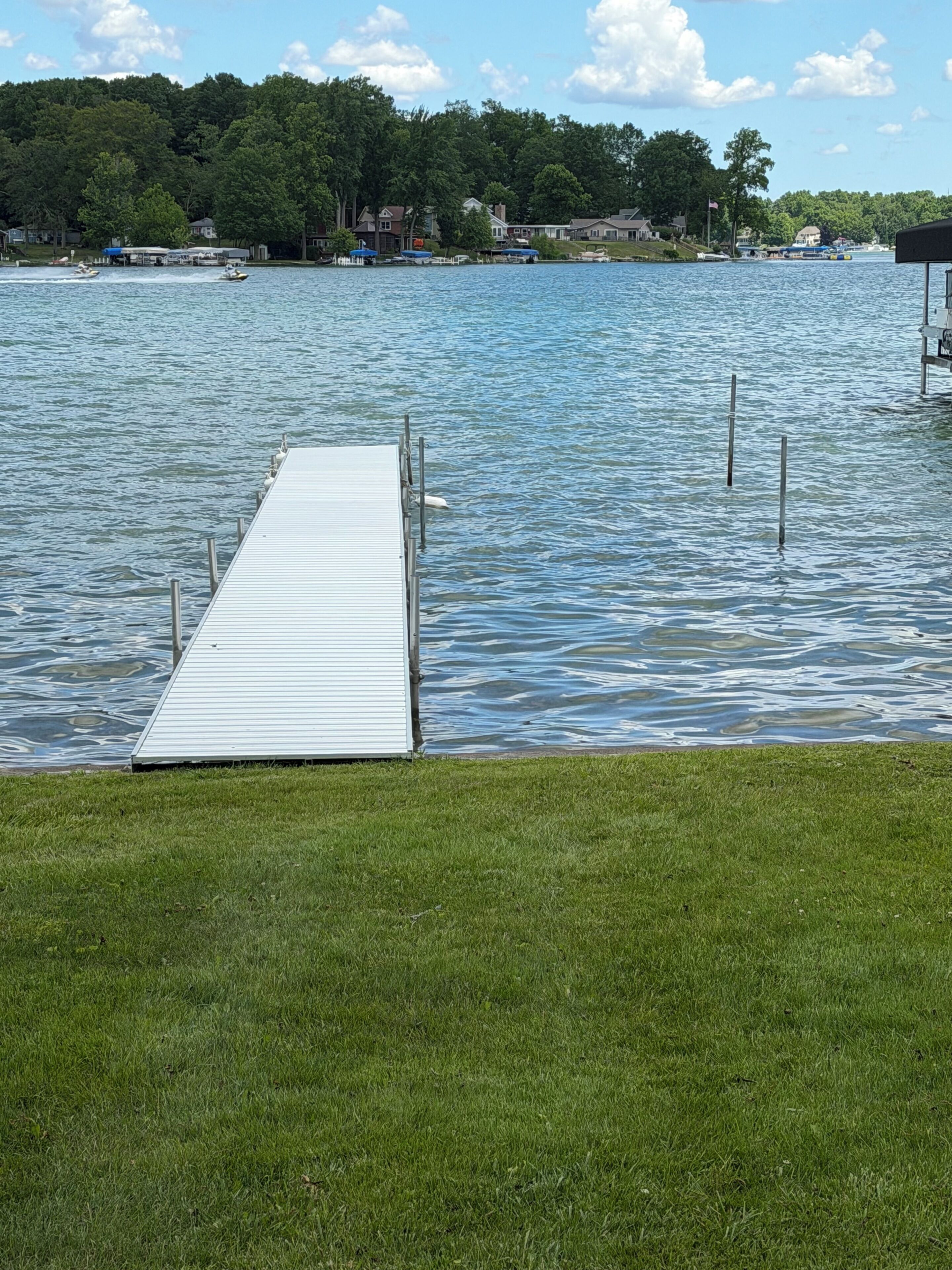 A dock extending into calm water with a grassy area in the foreground.