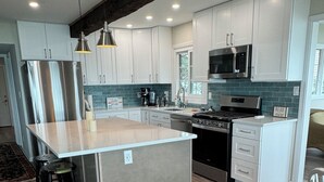 A modern kitchen with a central island, stainless steel appliances, and a patterned rug. - Notre Dame Football! 4-bedroom cottage on Diamond Lake! (Cassopolis)
