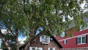 A brick house with a red roof, a paved driveway, and a large tree in the front yard. - Notre Dame Football! 4-bedroom cottage on Diamond Lake! (Cassopolis)