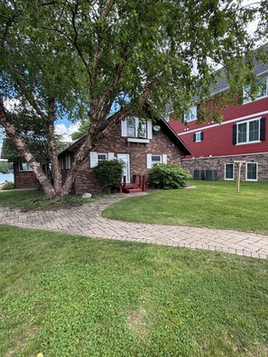 A brick house with a red roof, a paved driveway, and a large tree in the front yard.