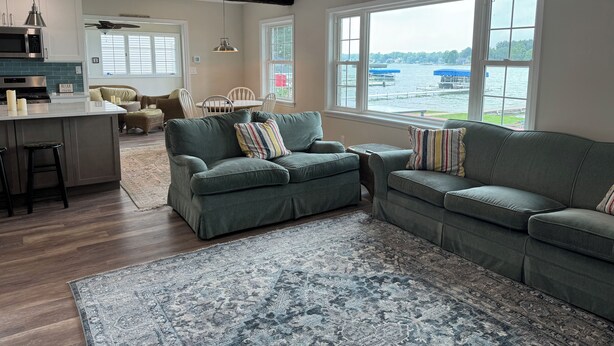 A spacious living area with a large window overlooking a body of water, a kitchen with modern appliances, and a cozy seating arrangement. - Notre Dame Football! 4-bedroom cottage on Diamond Lake! (Cassopolis)