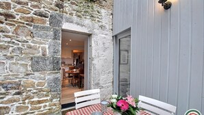 A stone exterior wall with a wooden deck and a table with a checkered tablecloth. - La Maison Gousset - GUINGAMP (GUINGAMP)