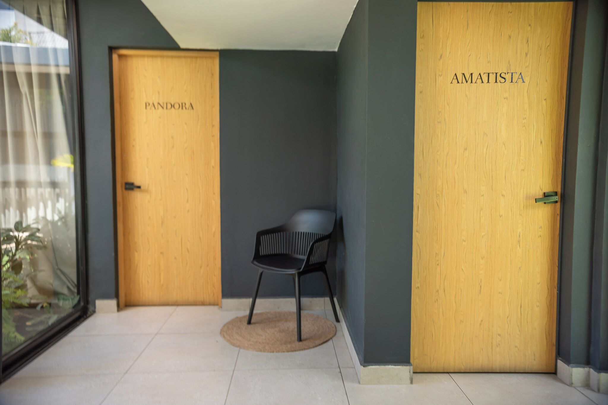 A hallway with two wooden doors labeled 'PANDORA' and 'AMATISTA'. A black chair is placed in the center.