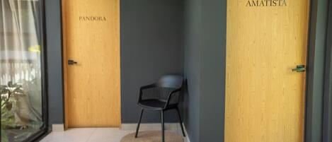 A hallway with two wooden doors labeled 'PANDORA' and 'AMATISTA'. A black chair is placed in the center.
