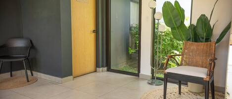 A modern interior with a sliding glass door leading to a balcony, a wicker chair, a small table, and a potted plant.