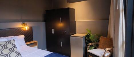 Un dormitorio con cama, armario, mesita de noche, silla, planta en maceta y equipo de aire acondicionado.