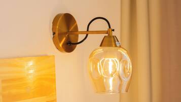A wall-mounted lamp with a clear glass shade, a wooden headboard, and a curtain.