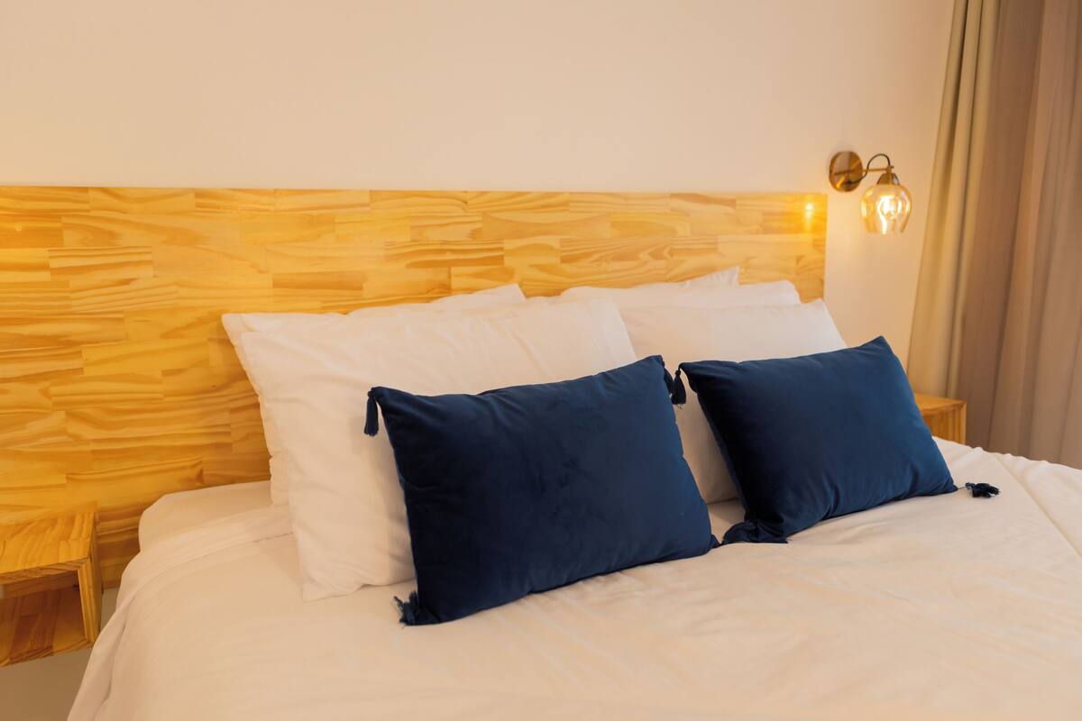 A neatly made bed with white and navy blue pillows, a wooden headboard, and a small bedside table.