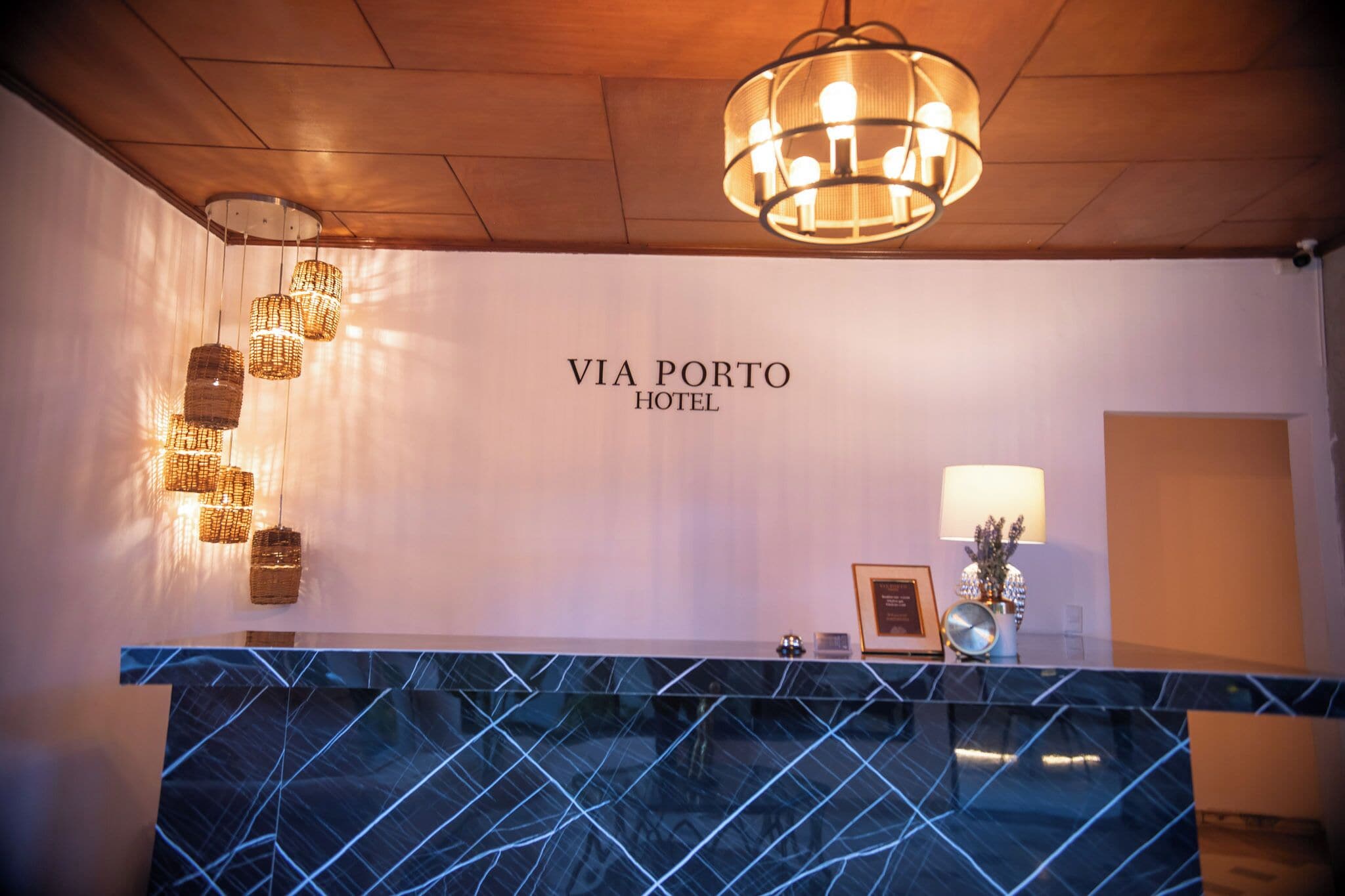 A reception desk with a marble top, a chandelier, and a wall sign that reads 'VIA PORTO HOTEL'.