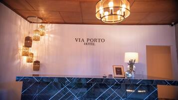 A reception desk with a marble top, a chandelier, and a wall sign that reads 'VIA PORTO HOTEL'.