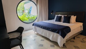 Een slaapkamer met een bed, een rond raam, een stoel en uitzicht op groen.