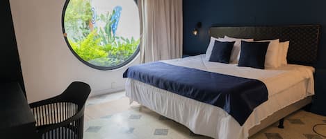 Un dormitorio con cama, un ventanal redondo, una silla y vistas al verdor.