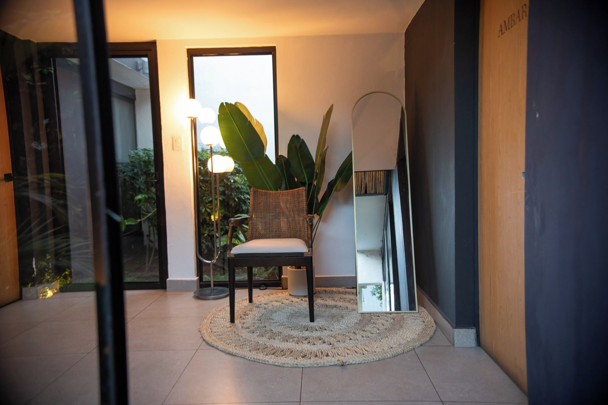 Una sala moderna con un tapete redondo, una silla, una planta grande y una lámpara de pie.