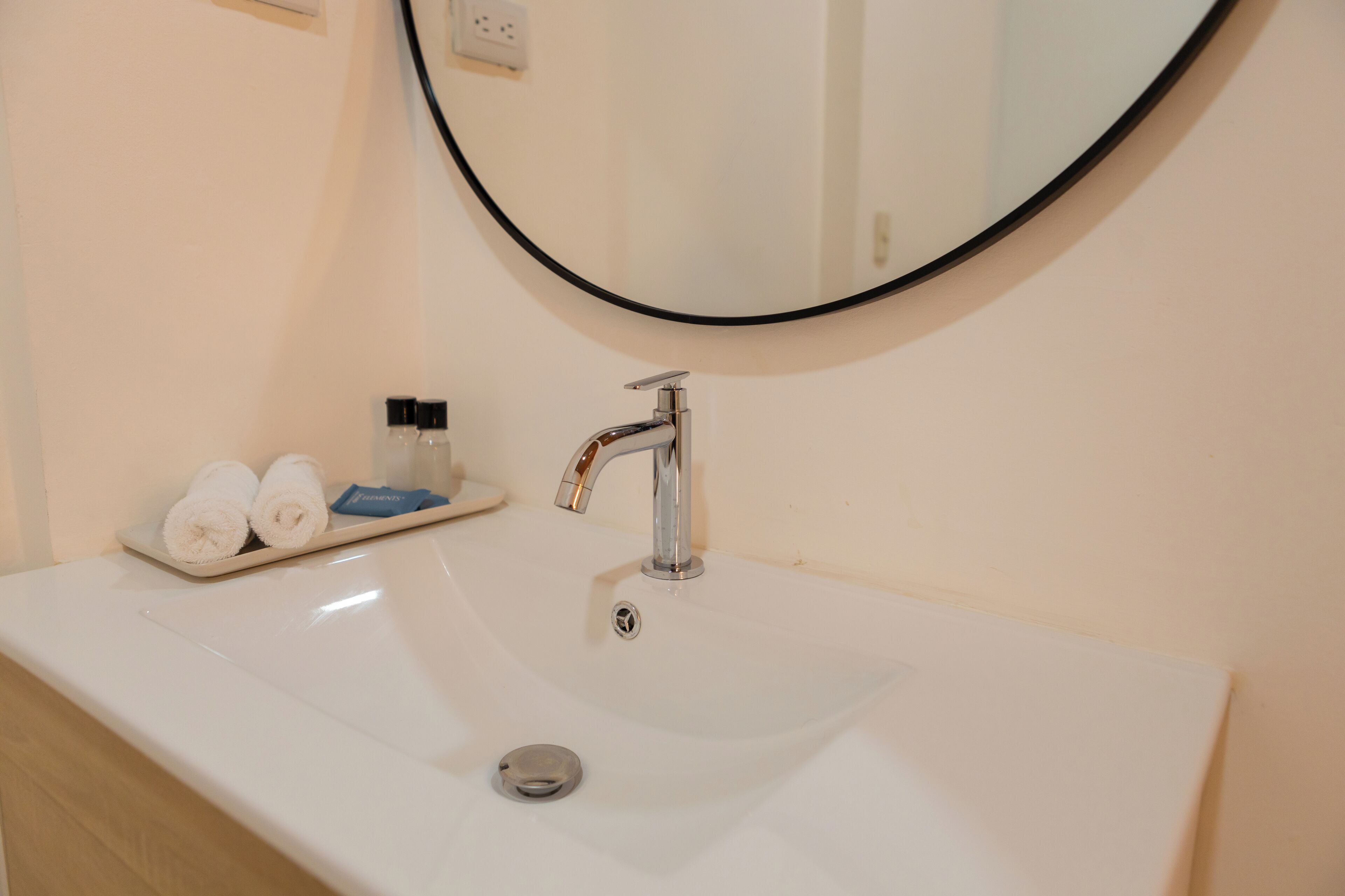 Een wit wastafelmeubel met een moderne kraan, een spiegel erboven en een dienblad met handdoeken en toiletartikelen.