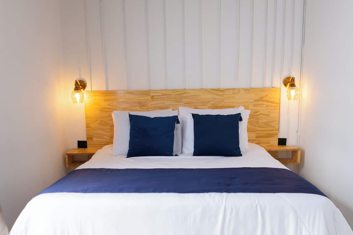 A neatly made bed with a wooden headboard, two bedside tables with lamps, and a patterned floor.