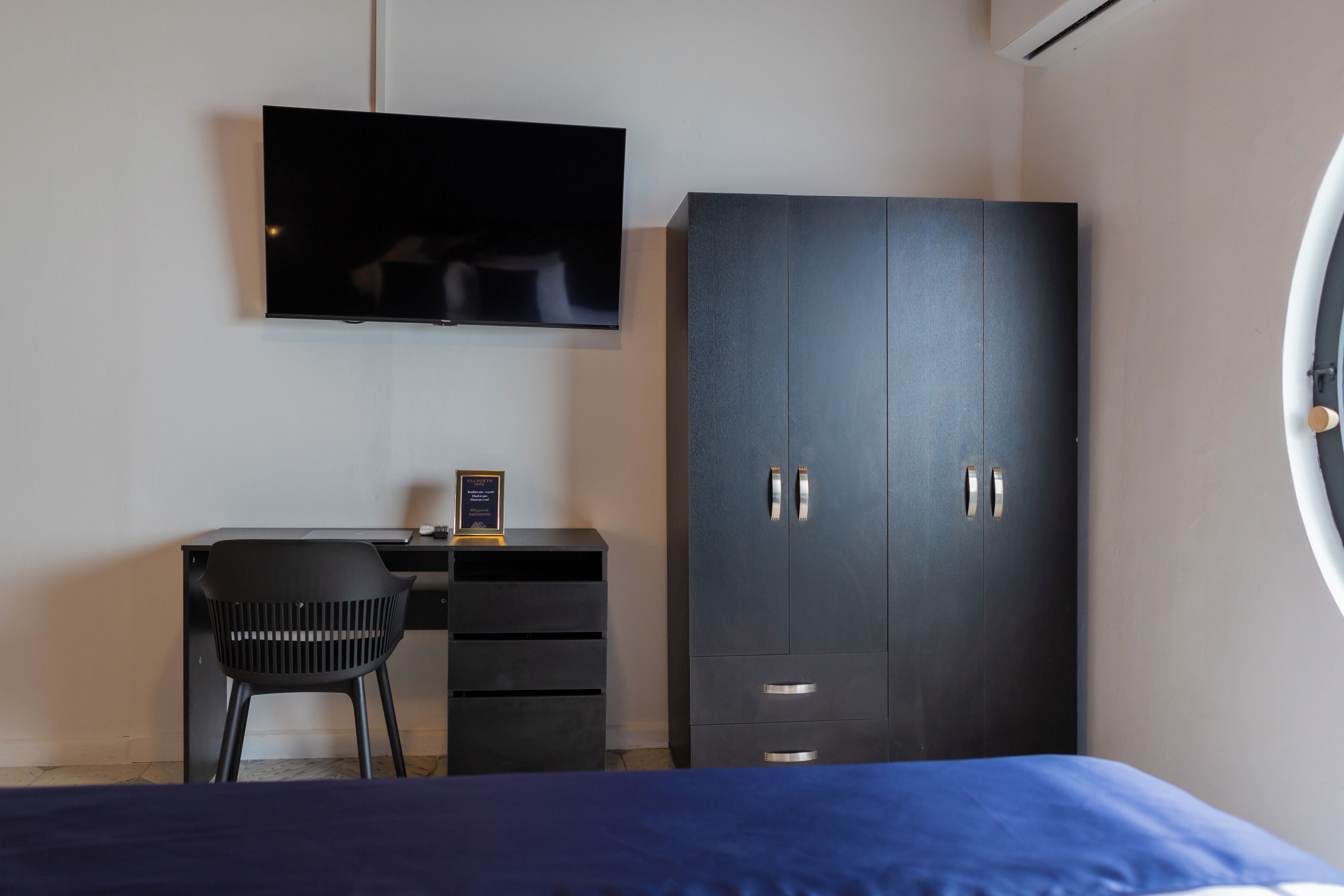 A bedroom with a bed, a desk with a chair, a wardrobe, and a television on the wall.