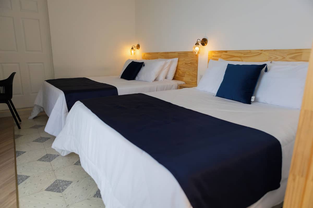 A hotel room with two beds, each with a wooden headboard and white bedding. There are wall-mounted light fixtures on either side of the beds.