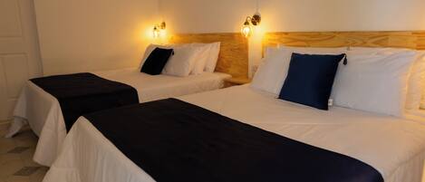 Zwei Einzelbetten mit weißen Laken und dunklen Kopfteilen, ein Holz-Kopfteil sowie Wandleuchten.