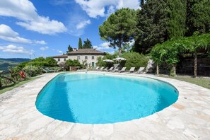 A swimming pool with a stone deck, surrounded by trees and a house in the background.