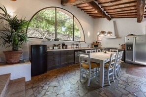 A kitchen with a stone floor, a large window, and a dining area with chairs. - Villa Poggio la Croce by MMega (Radda in Chianti)