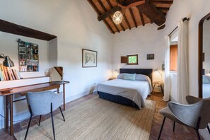 Ein Schlafzimmer mit Bett, Schreibtisch, Stühlen und einer Decke mit sichtbaren Holzbalken.