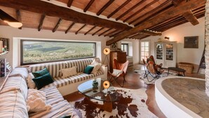 Un salón amplio con un gran ventanal, una mesa de centro de cristal, un sofá a rayas y una chimenea de piedra.