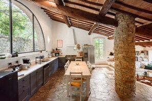 A rustic kitchen with stone flooring, a wooden dining table, and a stone pillar.