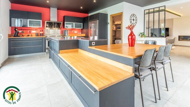 Una cocina moderna con una isla central, armarios oscuros y una pared de acento roja.