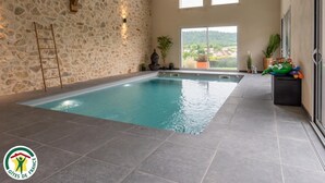 Una piscina interior con paredes de piedra, una escalera y vistas al exterior.