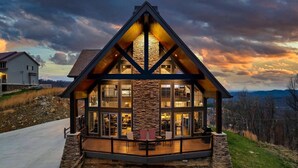Une maison moderne à plusieurs étages, dotée de grandes fenêtres et d’une façade en pierre, qui se distingue par son emplacement dans un cadre pittoresque.
