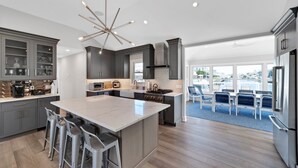 A modern kitchen with a central island, bar stools, and a view to a patio area. - Waterfront Mantoloking Home with Private Dock w/Pool very close to Ocean Beach  (Mantoloking)