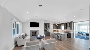 A spacious living area with a fireplace, grey upholstered furniture, and a kitchen with modern appliances. - Waterfront Mantoloking Home with Private Dock w/Pool very close to Ocean Beach  (Mantoloking)