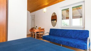 Ett rum med en blå soffa, ett träpanelat tak, ett matbord med stolar och ett fönster med persienner.