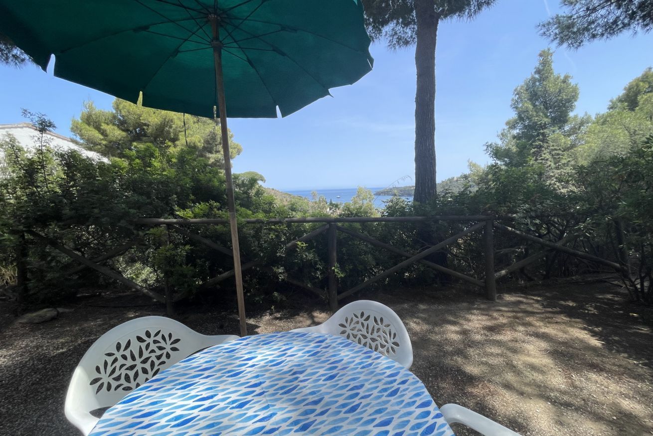 Ein Tisch mit einem gemusterten Tischläufer, einem grünen Sonnenschirm und Blick aufs Meer.