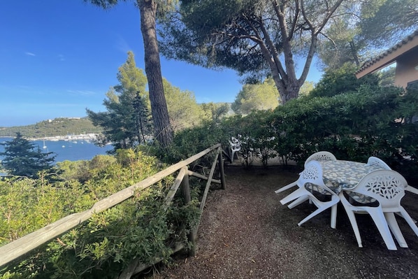 Un patio con sillas de plástico blanco y una mesa, rodeado de follaje y con vistas al litoral.