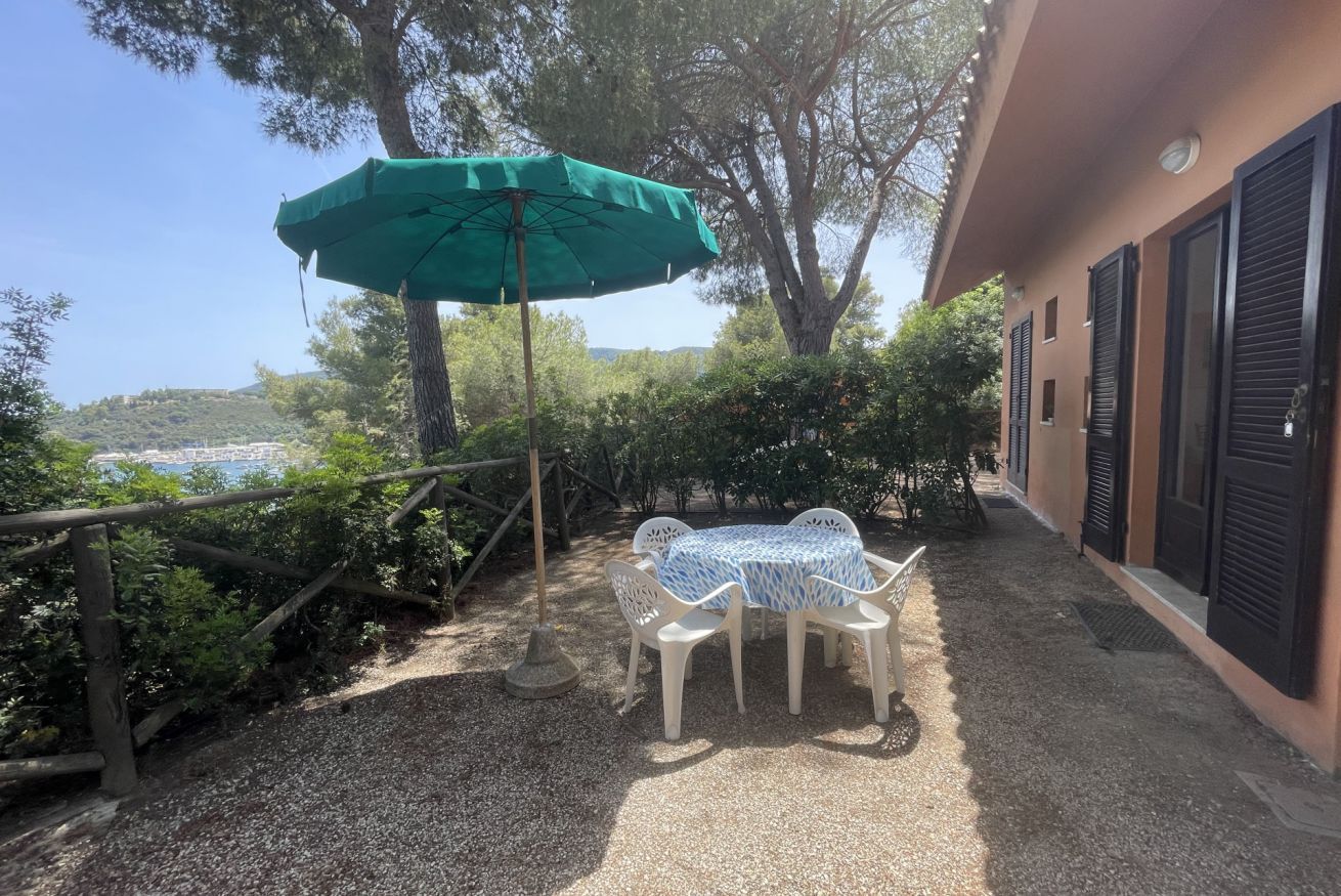 Une terrasse extérieure avec une table et des chaises, un parasol vert et une vue sur la mer.