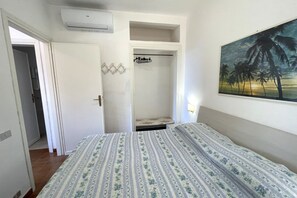 Un dormitorio con cama, aire acondicionado, armario y un cuadro de palmeras.