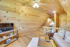 A cozy attic bedroom with wooden walls and a sloped ceiling. It features a large bed, a TV on a wooden stand, and a small table with a plant. - Home w/ Fire Pit on 27 Acres in Walhalla! (Walhalla)