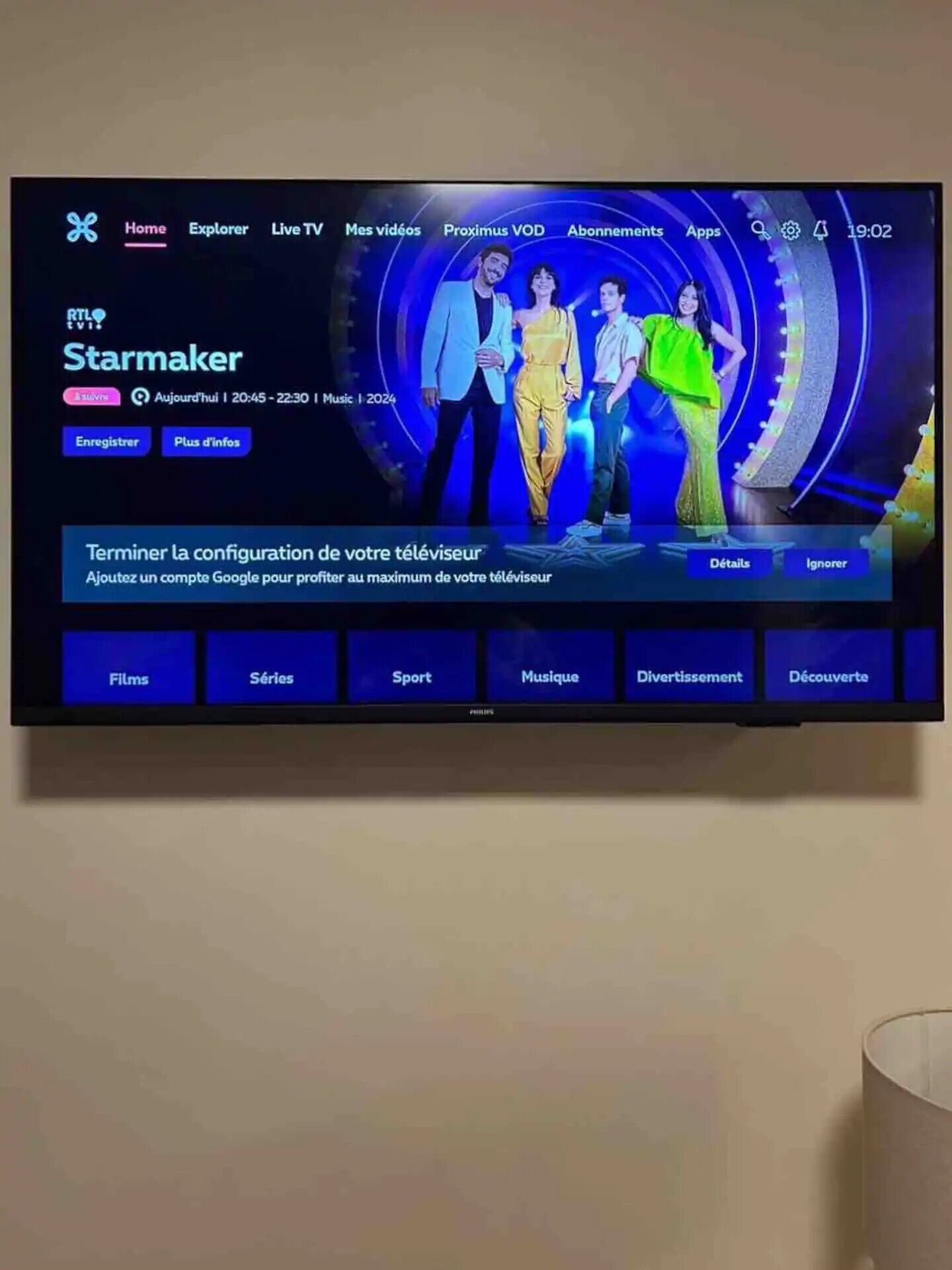 Ein Fernsehbildschirm zeigt eine Fernsehsender-Menüoberfläche mit Optionen wie Startseite, Entdecken, Live-TV und mehr.