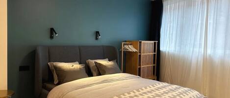 Un dormitorio con cama, mesita de noche, armario y una lámpara de pared.